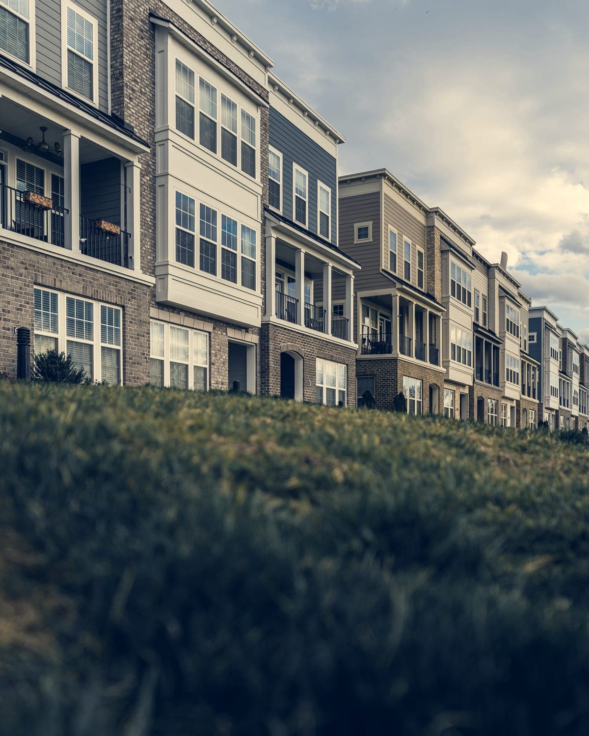 A row of three-storey brick and siding townhomes with bay windows, seen across a lawn